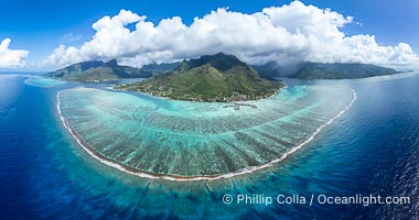 Barrier Reef around Moorea Island, French Polynesia. Cook's Bay to the left, Opunohu Bay to the right. The outer reef slope is seen adjacent to deep blue oceanic water with white waves breaking against the reef edge. Next, a wide shallow reef flat occurs dotted with coral bommies. Inside of that, a shallow protected lagoon is formed against the island.  Tall, rugged, eroded mountains are seen hinting at the age of the ancient volcano that originally formed the island and that is now sinking back down, leaving the encircling reef behind