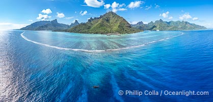 Barrier Reef around Moorea Island, French Polynesia. The outer reef slope is seen adjacent to deep blue oceanic water with white waves breaking against the reef edge. Next, a wide shallow reef flat occurs dotted with coral bommies. Inside of that, a shallow protected lagoon is formed against the island.  Tall, rugged, eroded mountains are seen hinting at the age of the ancient volcano that originally formed the island and that is now sinking back down, leaving the encircling reef behind