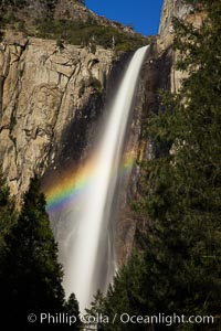 Bridalveil Falls with a rainbow forming in its spray, dropping 620' into Yosemite Valley, displaying peak water flow in spring months from deep snowpack and warm weather melt, Yosemite National Park, California