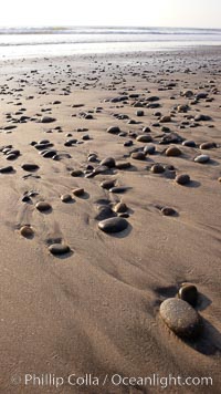 Cobblestones on a flat sand beach.  Cobble stones are polished round and smooth by years of wave energy.  They are alternately exposed and covered by sand depending on the tides, waves and seasons of the year.  Cobblestones are common on the beaches of southern California, contained in the sandstone bluffs along the beach and released onto the beach as the bluffs erode, Carlsbad