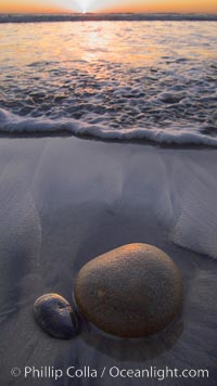 Cobblestone lies on the sand at the ocean's edge, sunset