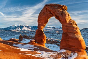 Delicate Arch, dusted with snow, at sunset, with the snow-covered La Sal mountains in the distance.  Delicate Arch stands 45 feet high, with a span of 33 feet, atop of bowl of slickrock sandstone, Arches National Park, Utah