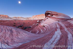 The moon sets over the Fire Wave, a beautiful sandstone formation exhibiting dramatic striations, striped layers in the geologic historical record, Valley of Fire State Park