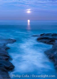 Breaking waves crash upon a rocky reef under the light of a full moon, La Jolla, California