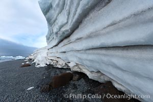 Horizontal striations and layers in packed snow, melting and overhanging, seen from the edge of the snowpack, along a rocky beach, Brown Bluff