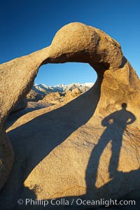 The long shadow of a hiker lies on Mobius Arch, a natural stone arch in the Alabama Hills, Alabama Hills Recreational Area