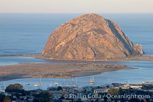 Morro Rock lit at sunrise, rises above Morro Bay which is still in early morning shadow
