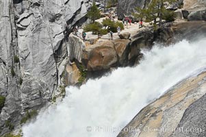 The brink of Nevada Falls, with hikers visible at the precipice. Nevada Falls marks where the Merced River plummets almost 600 through a joint in the Little Yosemite Valley, shooting out from a sheer granite cliff and then down to a boulder pile far below, Yosemite National Park, California