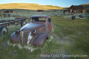 Old car lying in dirt field, Fuller Street and Green Street buildings in background, Bodie State Historical Park, California