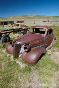 Old car lying in dirt field, Fuller Street and Green Street buildings in background, Bodie State Historical Park, California