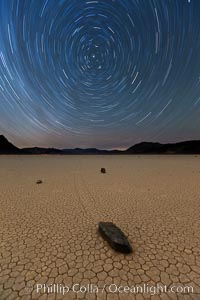 Racetrack sailing stone and star trails.  A sliding rock of the Racetrack Playa. The sliding rocks, or sailing stones, move across the mud flats of the Racetrack Playa, leaving trails behind in the mud. The explanation for their movement is not known with certainty, but many believe wind pushes the rocks over wet and perhaps icy mud in winter, Death Valley National Park, California