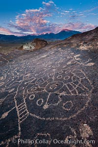 Sky Rock petroglyphs near Bishop, California, sunrise light just touching clouds and the Sierra Nevada. Hidden atop an enormous boulder in the Volcanic Tablelands lies Sky Rock, a set of petroglyphs that face the sky.  These superb examples of native American petroglyph artwork are thought to be Paiute in origin, but little is known about them