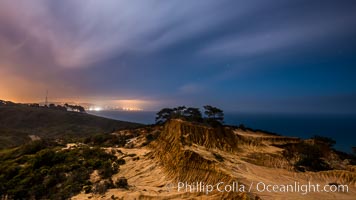Torrey Pines State Reserve at Night, stars and clouds fill the night sky with the lights of La Jolla visible in the distance, San Diego, California