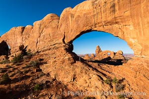 Tracy greets the dawn, with Turret Arch in the distance viewed through North Window at Sunrise, Arches National Park, Utah