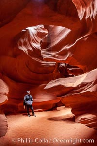 A hiker admiring the striated walls and dramatic light within Antelope Canyon, a deep narrow slot canyon formed by water and wind erosion, Navajo Tribal Lands, Page, Arizona