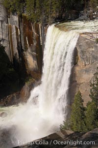 Vernal Falls at peak flow in late spring.  Hikers are visible at the precipice of the waterfall.  Viewed from the John Muir Trail.  Vernal Falls drops 317 through a joint in the narrow Little Yosemite Valley, Yosemite National Park, California