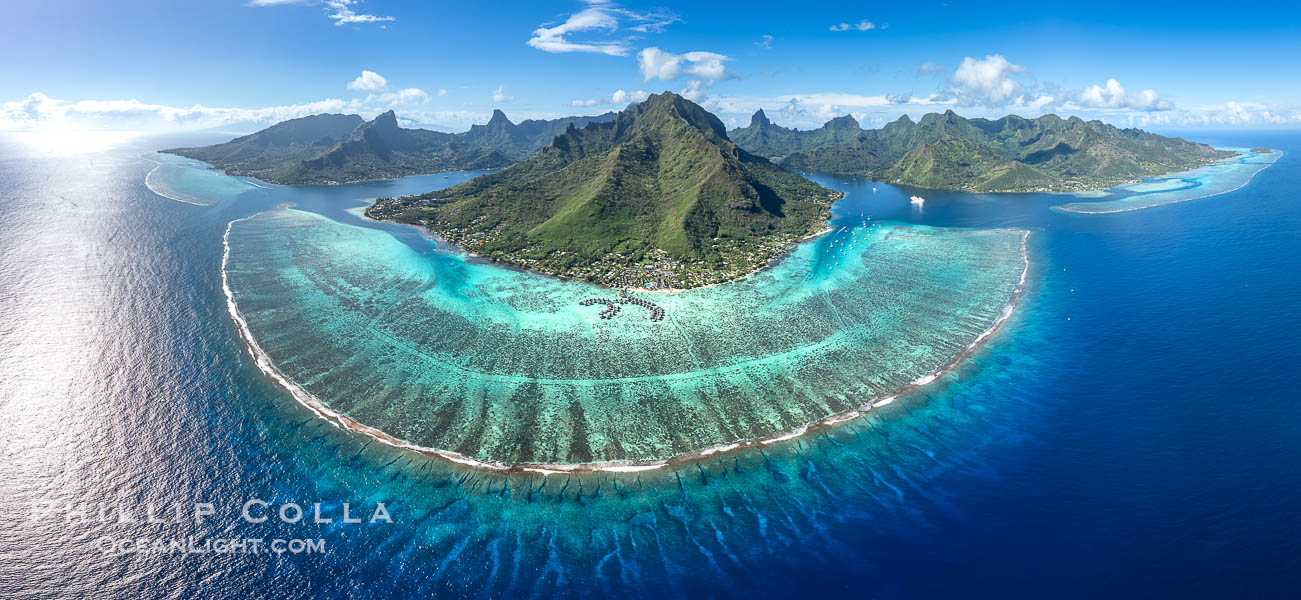 Barrier Reef around Moorea Island, French Polynesia. Cook's Bay to the left, Opunohu Bay to the right. The outer reef slope is seen adjacent to deep blue oceanic water with white waves breaking against the reef edge. Next, a wide shallow reef flat occurs dotted with coral bommies. Inside of that, a shallow protected lagoon is formed against the island.  Tall, rugged, eroded mountains are seen hinting at the age of the ancient volcano that originally formed the island and that is now sinking back down, leaving the encircling reef behind. France, natural history stock photograph, photo id 40676